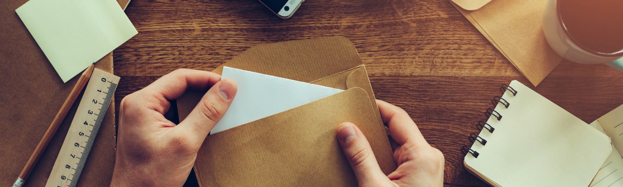 Person stuffing envelopes on a brown table with other papers and envelopes next to it