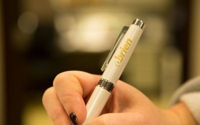 person holding a white pen that has a gold O'Brien logo on the pen cap