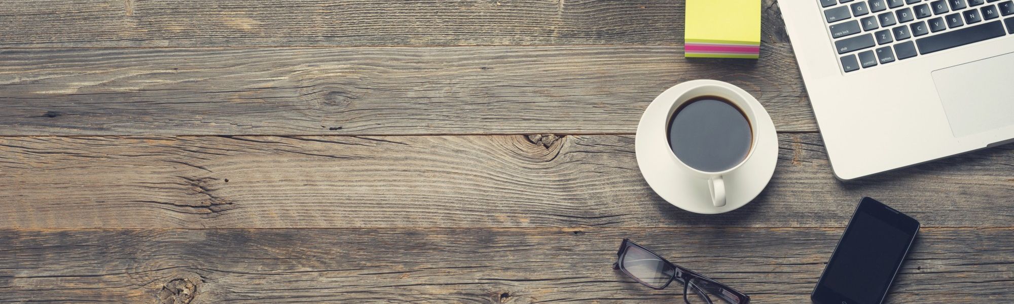 Wooden table with an apple computer, clickboard, cup of coffee, pencils and notepads on it