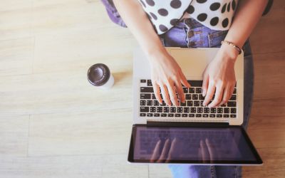 woman typing on a laptop on the floor with a cup of coffee next to her