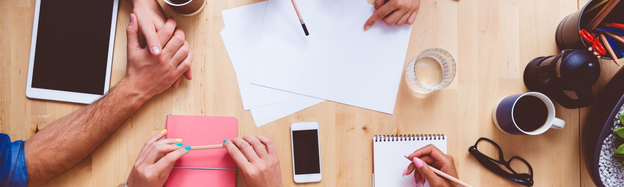 group of people working around a table together with pencils, cell phones, tablets, and notepads