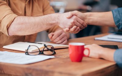 Two people sitting together at a wooden table having a discussion and shaking hands