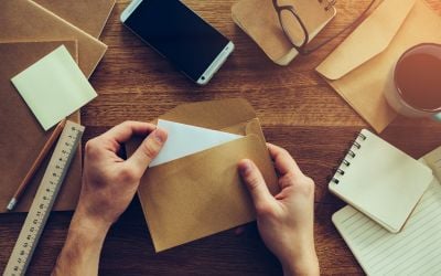 Person stuffing envelopes on a brown table with other papers and envelopes next to it