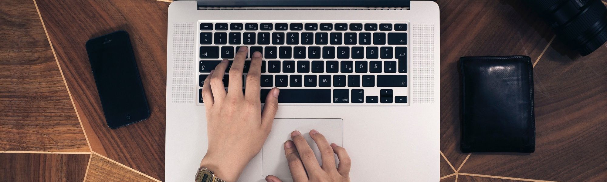 Hands typing on a computer on a wooden table.