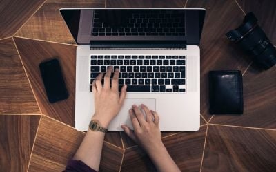 Hands typing on a computer on a wooden table. 